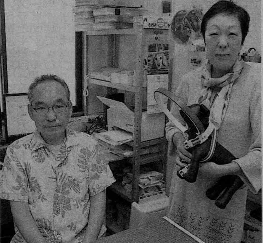 3Dプリンター前に立つ西澤夫婦の新聞掲載写真